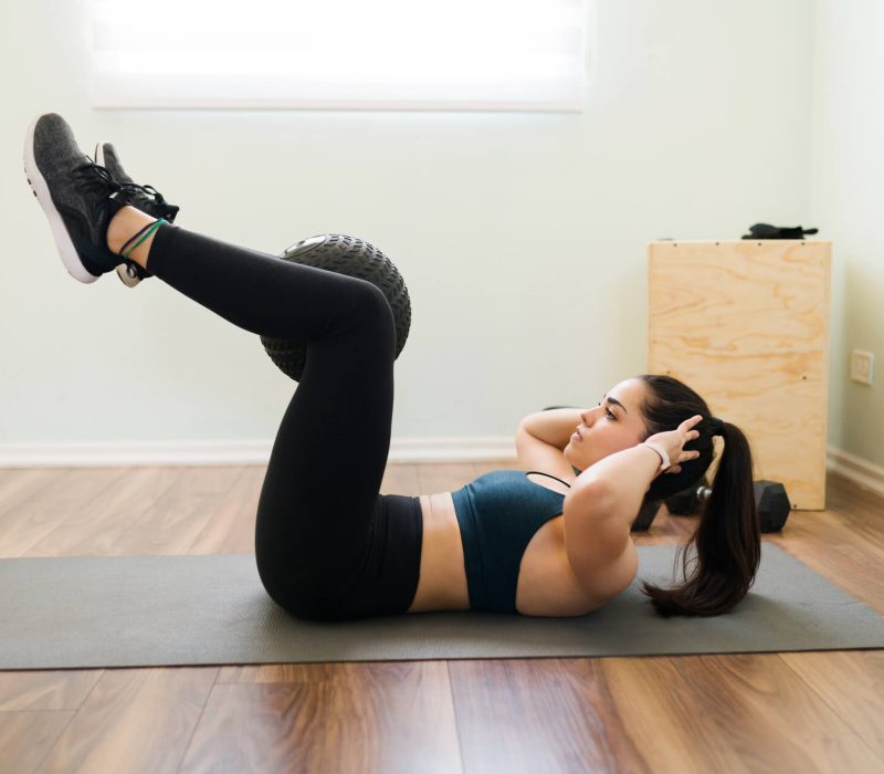 side-view-determined-young-woman-holding-slam-ball-with-her-legs-doing-abdominal-crunches-have-flat-abs